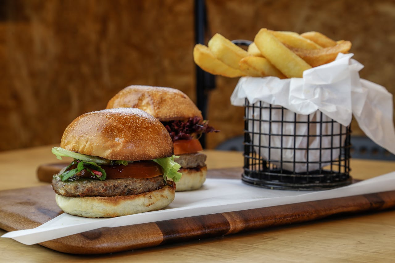 Close-up of appetizing burgers with fries served on a wooden board.